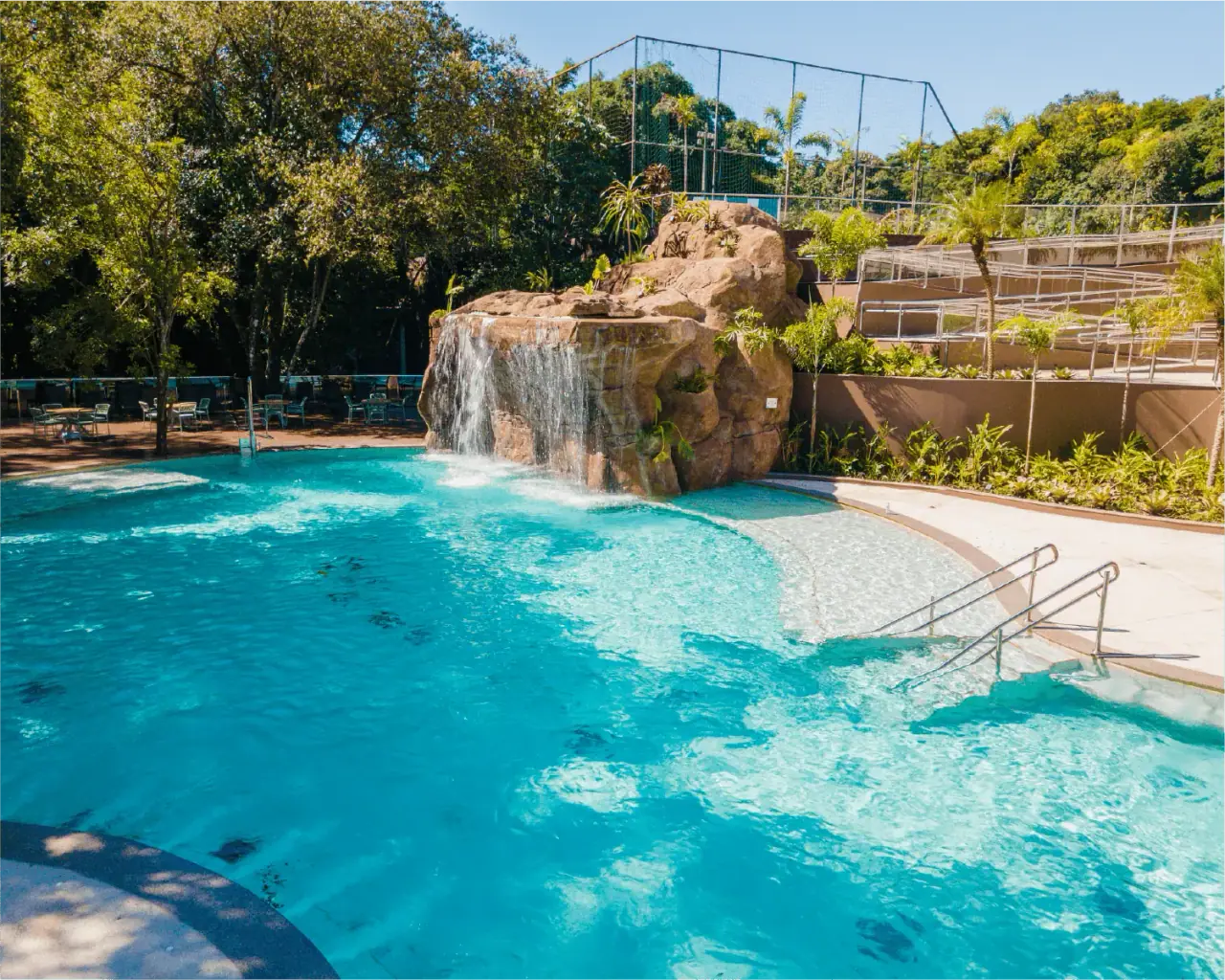 Piscina com cascata entre pedras e vegetação